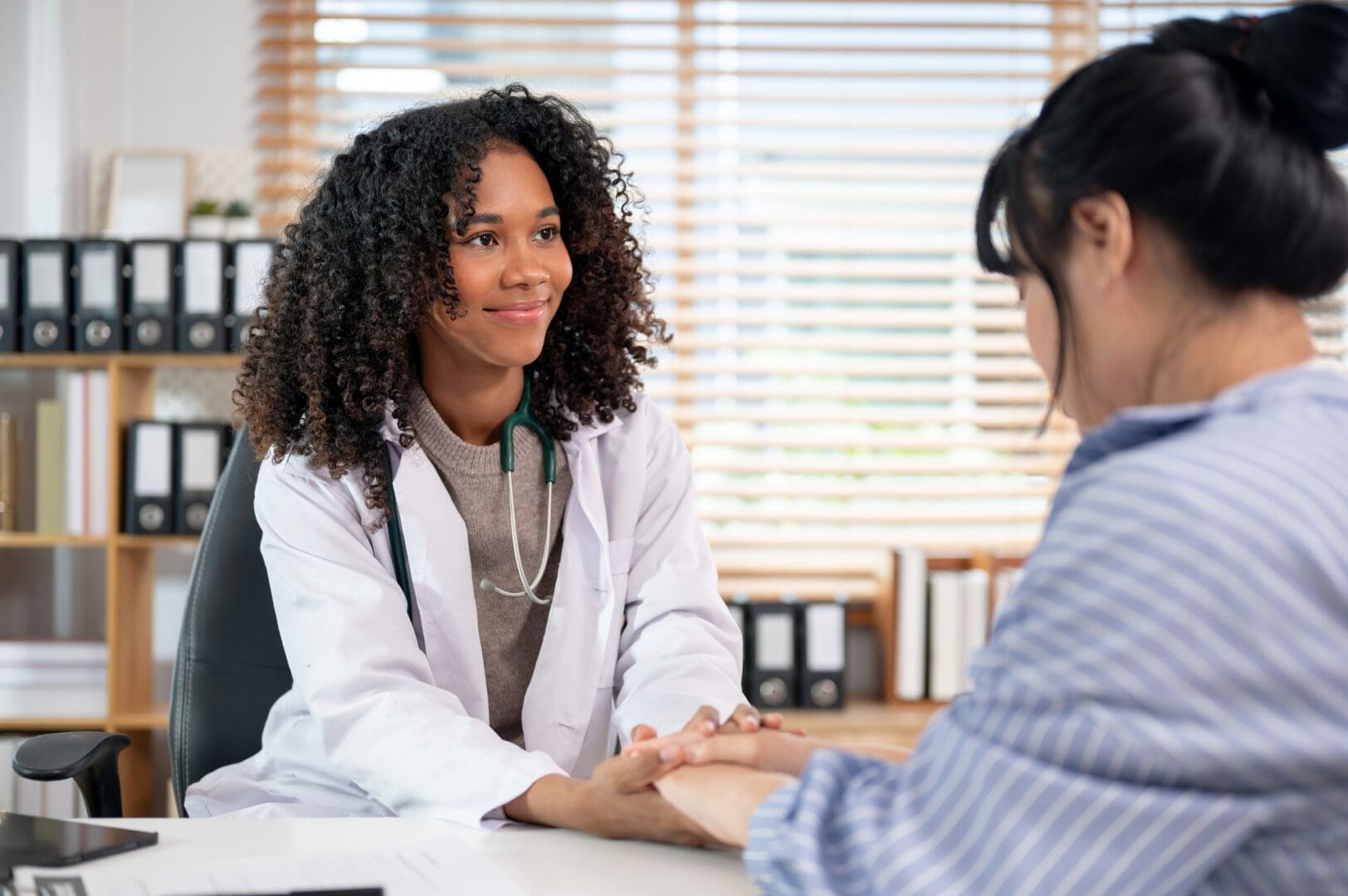 A caring Black female doctor holding a patient's hand to comfort and reassure them during a medical consultation in the examination room at the hospital.