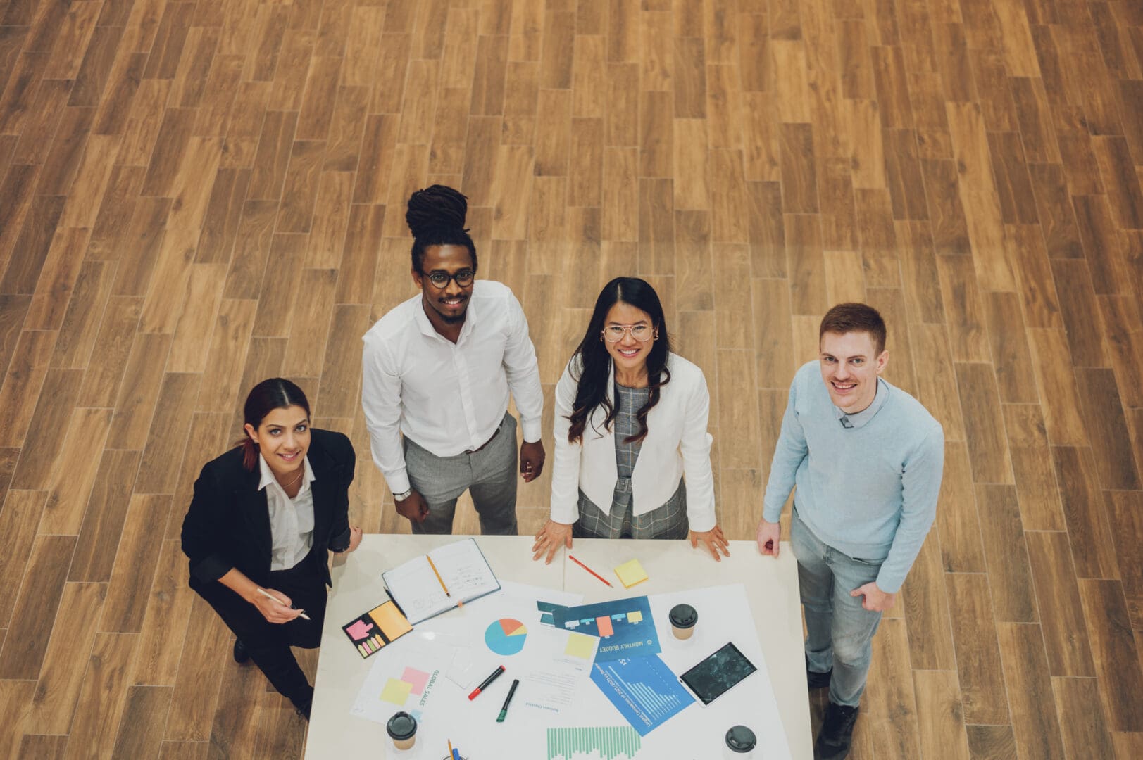 High angle shot of a happy multiracial business team working together at corporate briefing gathered at table in the conference room. Diverse colleagues in a boardroom. Looking into the camera.