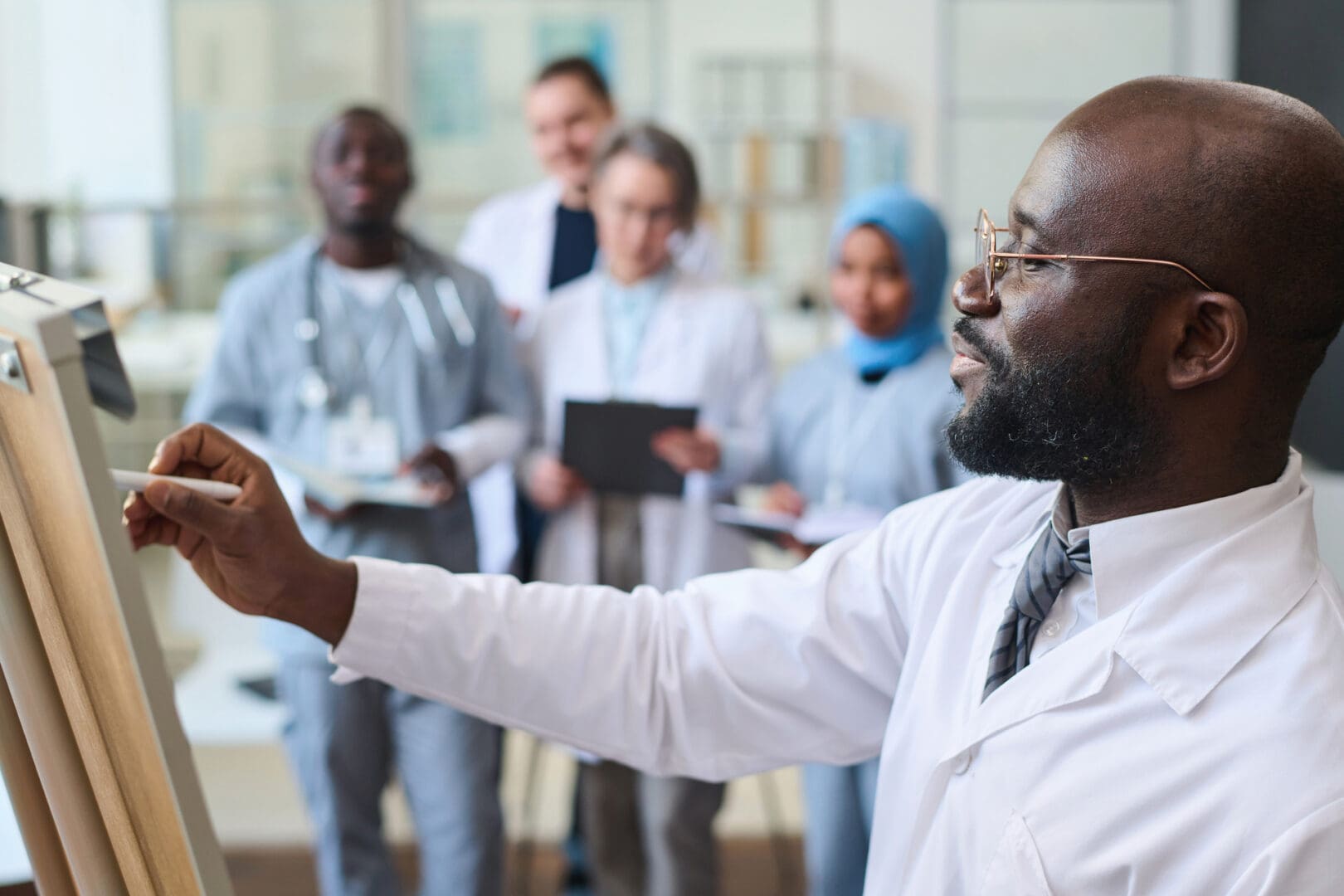 African American doctor writing on whiteboard and giving presentation to colleagues at seminar in office